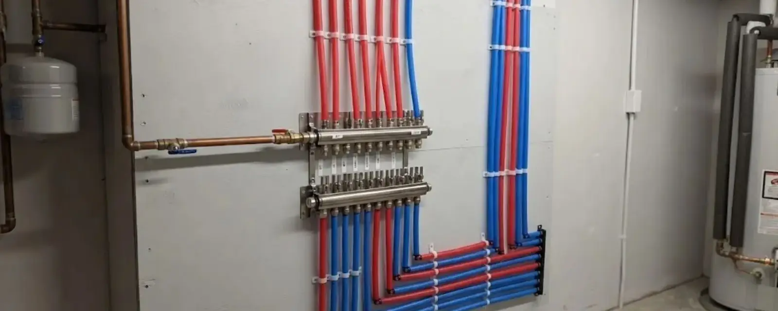 Red and blue PEX supply lines running from a manifold on a basement wall